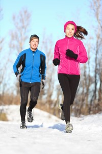 15589201 - young couple running dressed warmly in fleeces and gloves jogging in sunshine across winter snow in the countryside