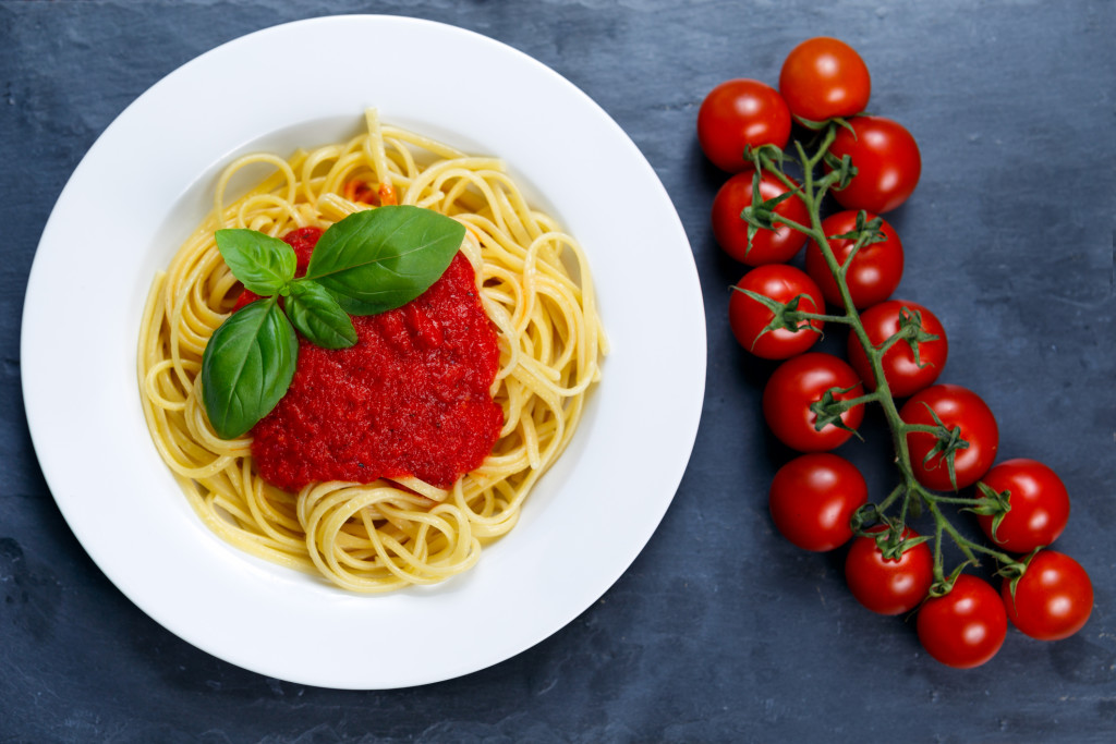 Spaghetti with marinara sauce and basil leaves on top, decorated with cherry tomatoes. on blue background.